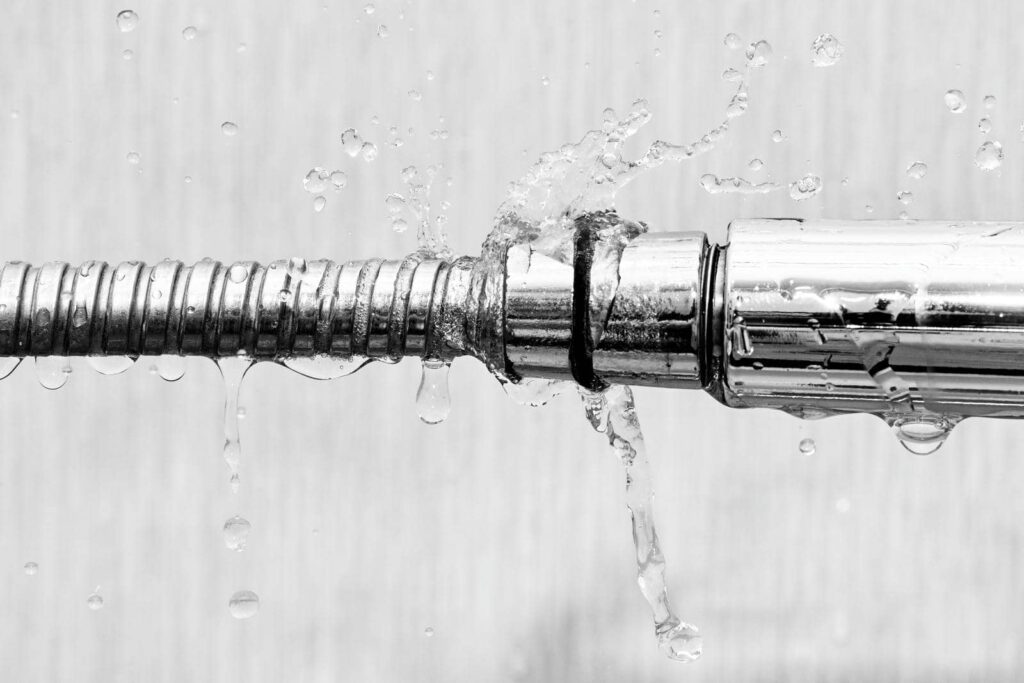 Water leaking and splashing from a broken metal pipe joint.