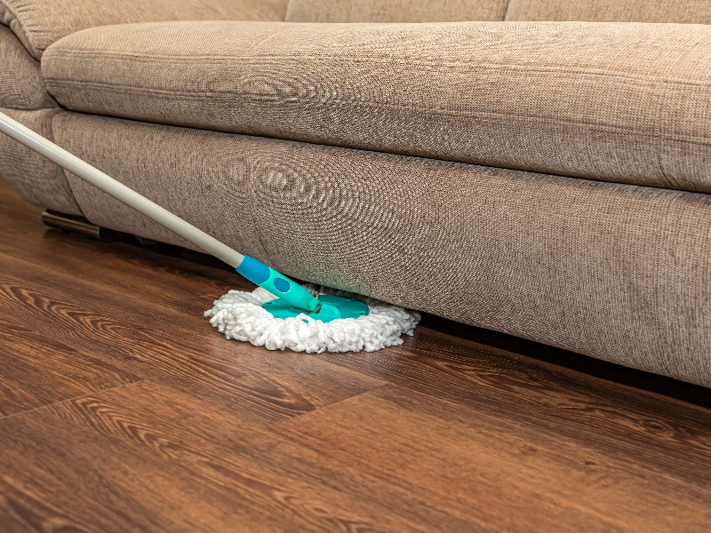 Microfiber mop cleaning hardwood floor under a beige fabric sofa. tenant trash out service